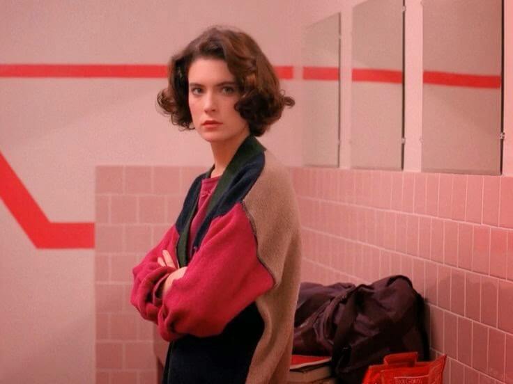 Woman in a colorful vintage sweater stands confidently in a retro pink bathroom.