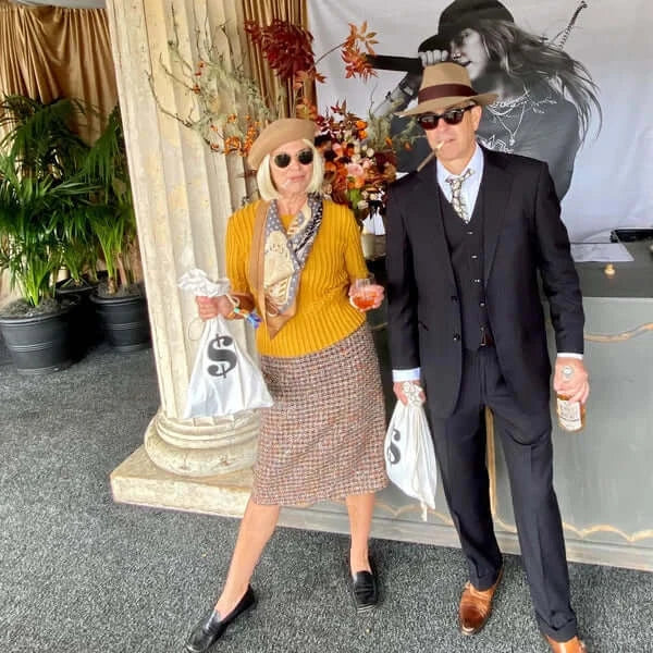 Stylish couple in retro attire, woman in mustard sweater and man in a suit holding shopping bags.