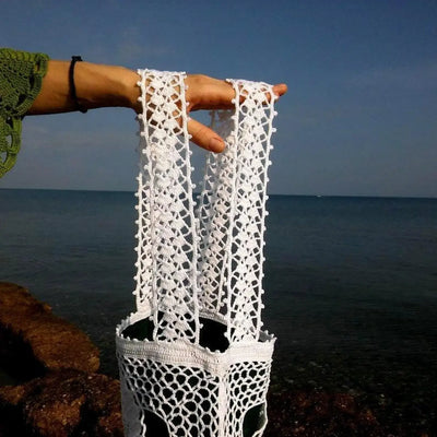 White crochet tote bag with openwork two-sided handles against a beach background.