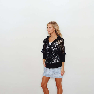 Black lace hooded crochet bomber jacket worn with denim skirt, perfect for summer style.