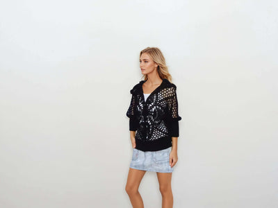 Stylish woman wearing a black lace hooded crochet bomber jacket with pineapple pattern, paired with a denim skirt.