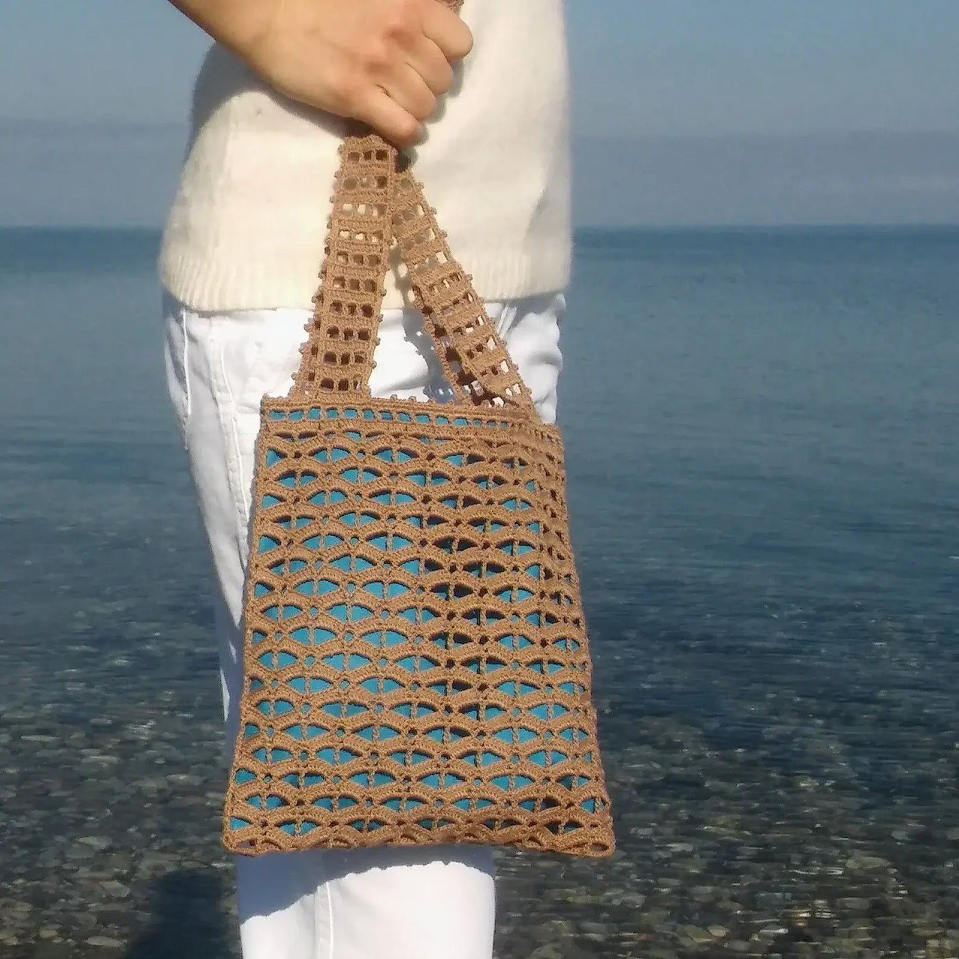 Small handmade brown crochet tote bag with geometric mesh pattern and blue lining, featuring short handles for comfort.