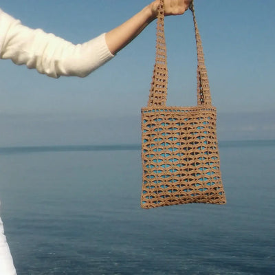 Hand holding a small handmade brown crochet tote bag with geometric mesh pattern, perfect for stylish and comfortable carrying.