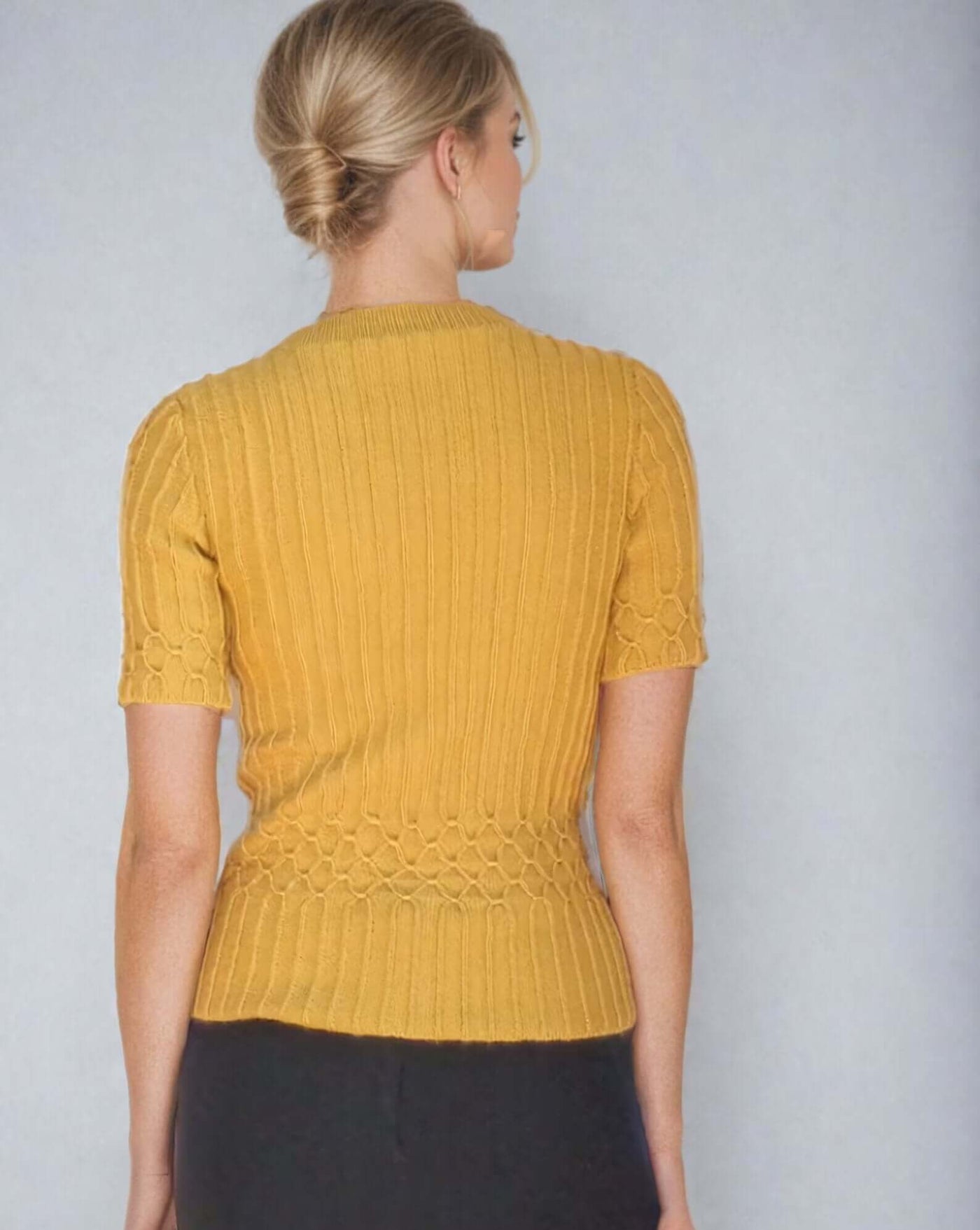 Back view of a mustard yellow cable knit women's sweater with short sleeves and intricate detailing.