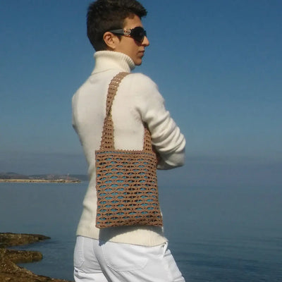 Woman wearing a small brown crochet tote bag with geometric mesh pattern and blue lining by the water.