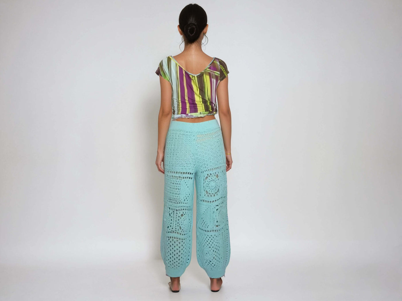 Back view of a model wearing turquoise high-waisted harem pants with a crochet granny square pattern.