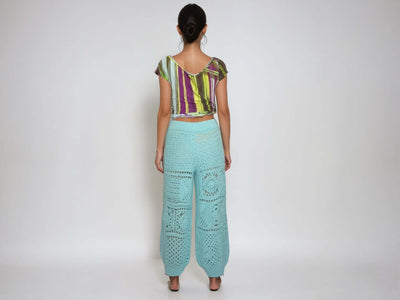 Back view of a model wearing turquoise high-waisted harem pants with a crochet granny square pattern.